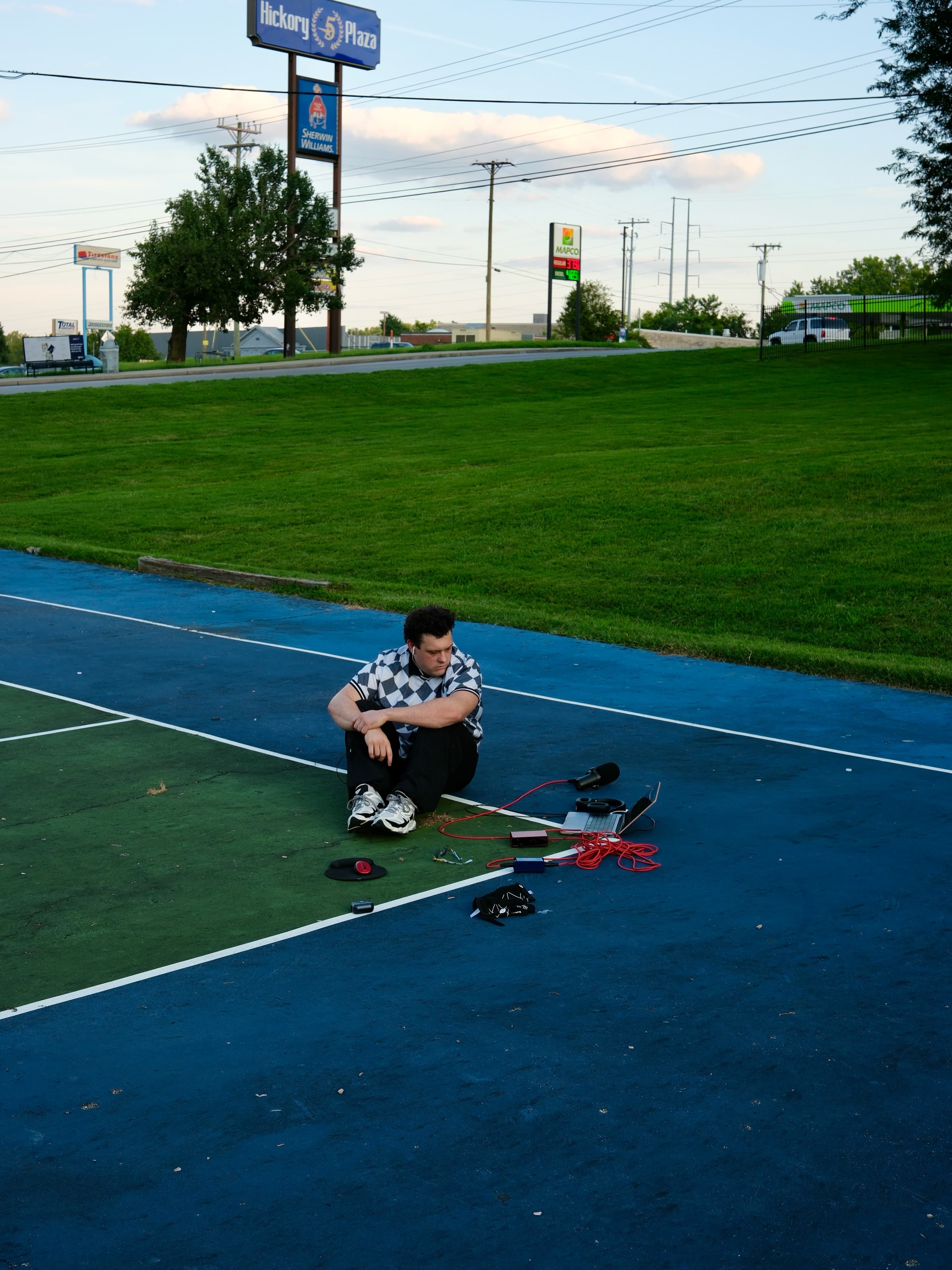 BRAVEN sitting on a blue outdoor court beside a microphone, laptop, and red audio cables.